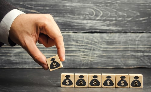 Hand laying down wooden blocks with money bags on them