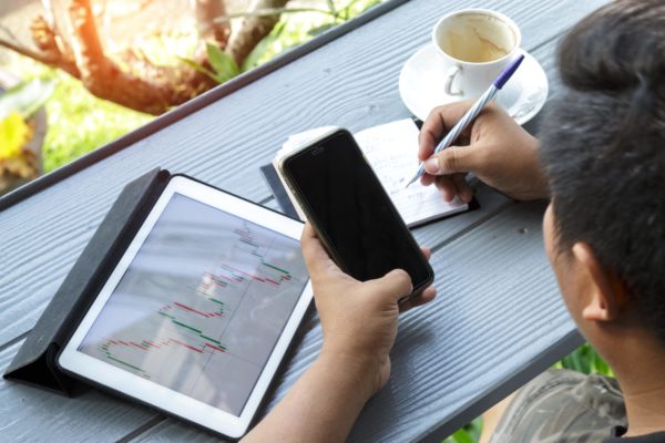 A man taking notes while looking at his phone and tablet