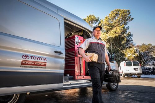 A Toyota forklift technician carrying parts from his service van