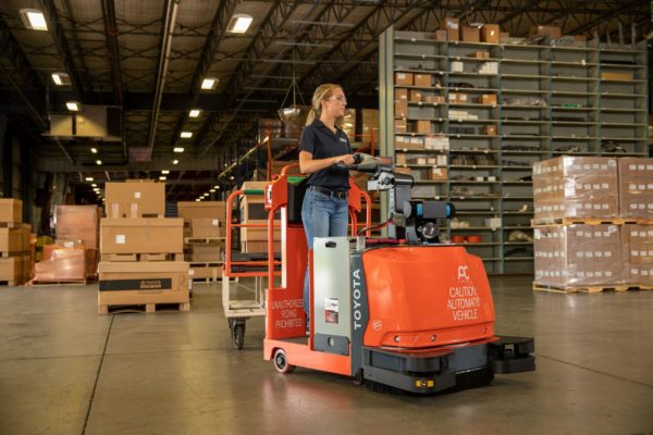 A worker on a Toyota AGV tow tractor hauling a cart