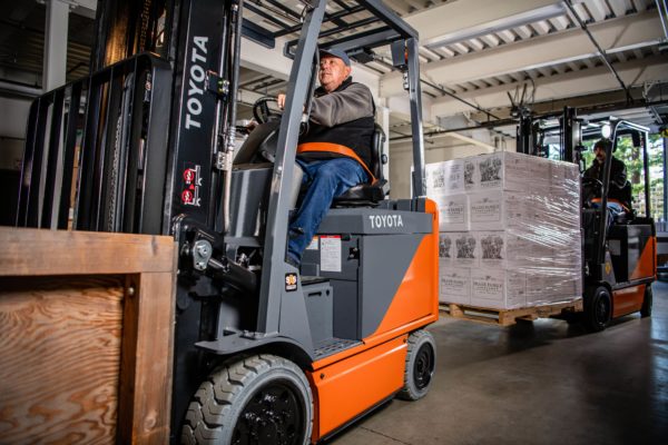 Two operators driving Toyota 4-wheel electric forklifts through a loading dock