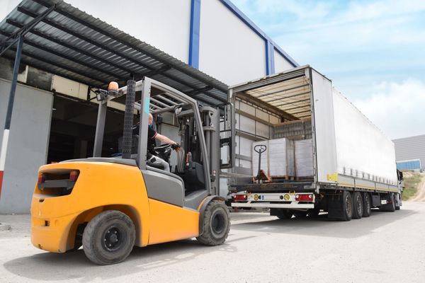 An orange internal combustion forklift unloading a semi-trailer