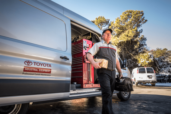 A Toyota forklift service technician walking with tools away from a service van