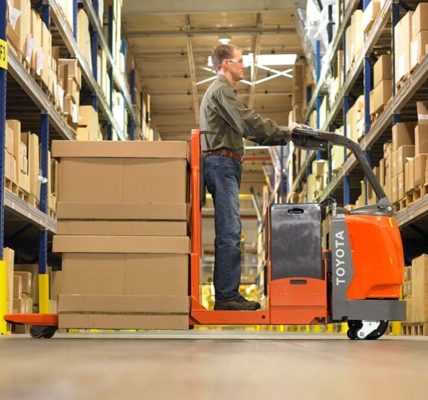 A worker on a pallet jack in the middle of a warehouse aisle