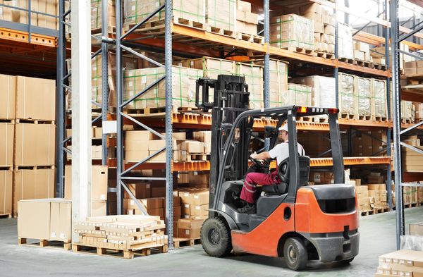 An orange forklift inside a warehouse with a worker walking past it