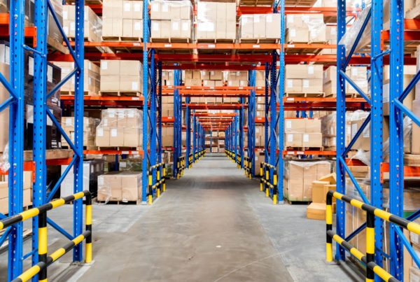 Looking down the aisle of a warehouse with pallet racking on either side and up top