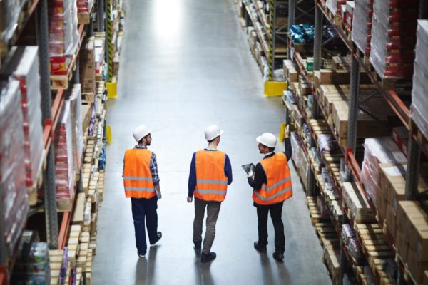 Three warehouse workers talking to each other as they walk down an aisle