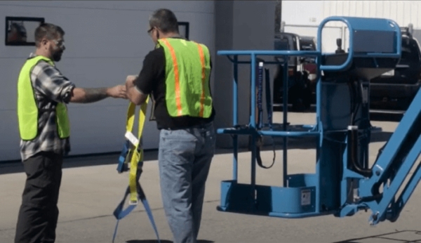 An aerial lift trainer handing an operator a body harness