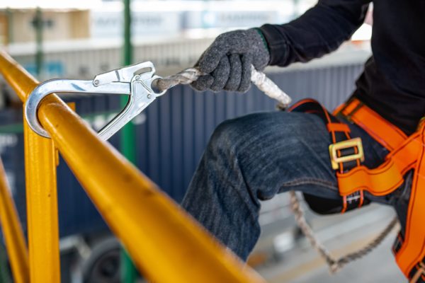 A worker in a body harness attaching a lanyard to a tie-off point