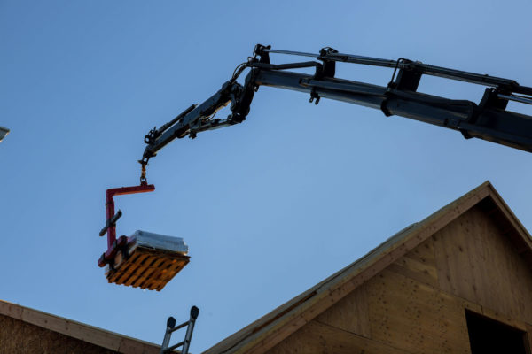 A boom arm with a fork attachment lifting a pallet of materials onto a roof