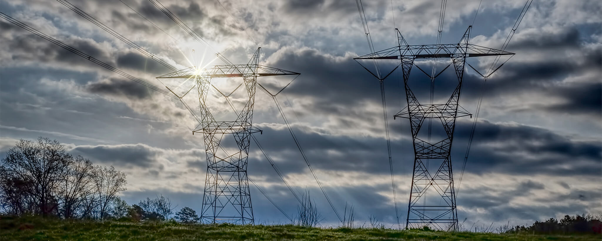 A pair of electrical power line towers with the sun shining in the background