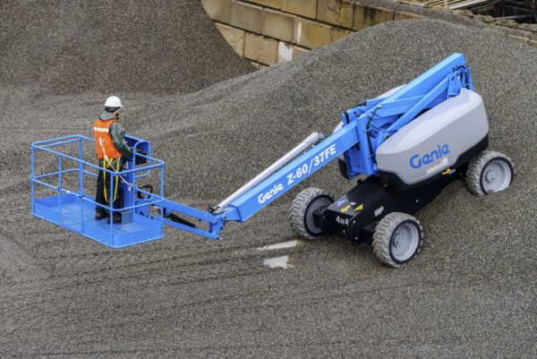 A Genie boom lift driving on a gravel pile