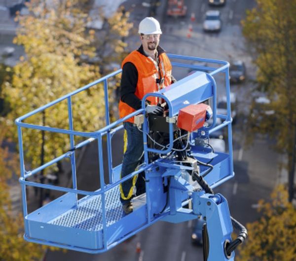 A Genie boom lift operator in a basket lifted in the air