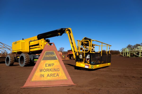 A boom lift parked near a warning sign indicating that the area is reserved for elevated work platforms