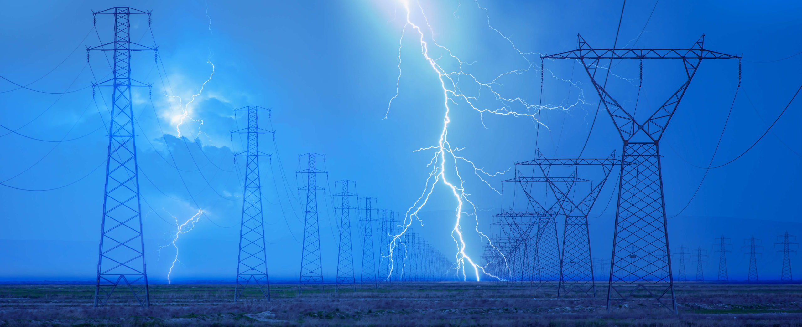 Lightning striking in a field between two rows of power line towers