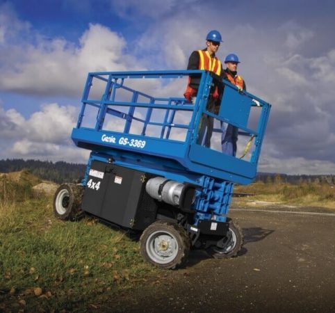 Two operators driving a Genie scissor lift down a small grassy hill