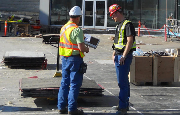 Two workers on a construction site discussing papers