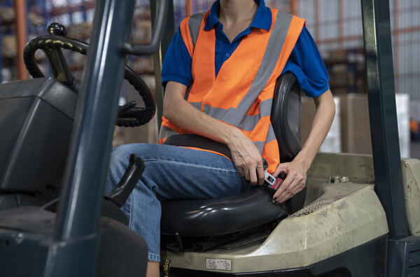 A forklift operator buckling their seat belt