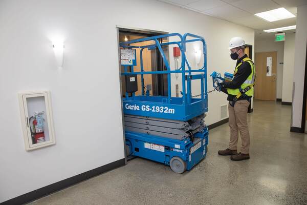 A boom lift operator using the ground controls to move a Genie scissor lift into an elevator