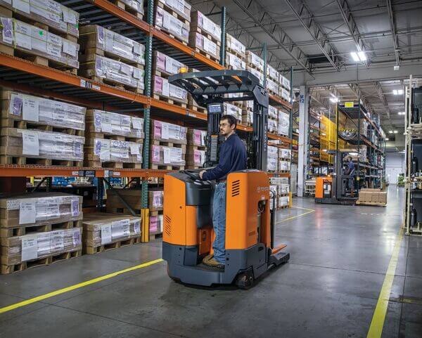 A reach truck operator driving down an aisle while looking backward