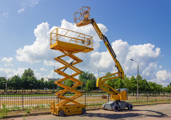 A scissor lift parked next to a boom lift outside