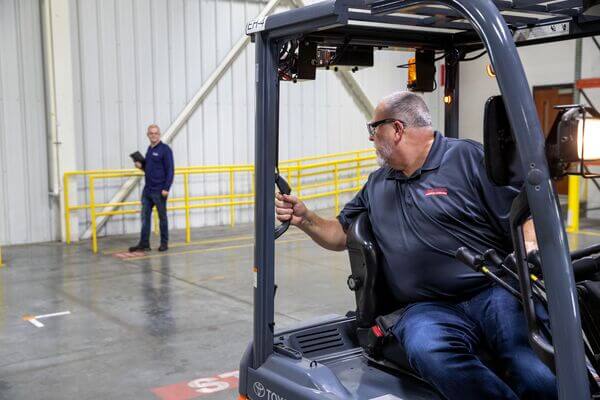 A sit-down forklift operator turning their neck to see backwards while reversing