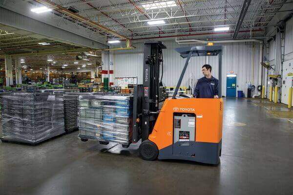 A stand-up forklift operator carrying a pallet inside a warehouse