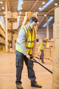 Male worker using pallet jack in distribution warehouse