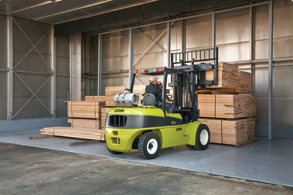 An operator lifting a stack of lumber using a CLARK sit-down forklift