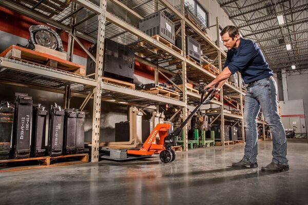 An operator lifting a pallet of forks using a hand pallet jack