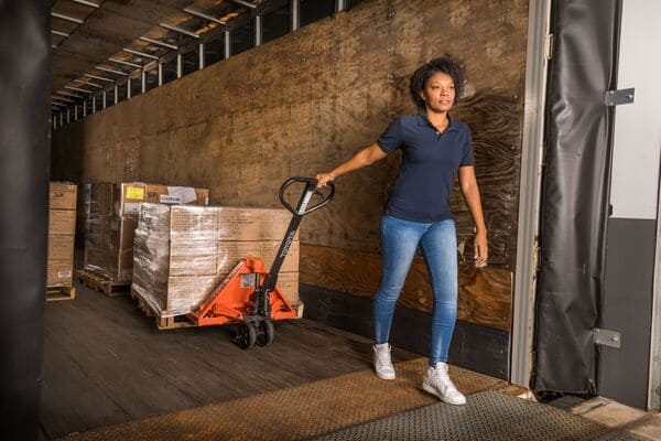 A worker using a Toyota hand pallet jack to remove a pallet from a semi-trailer