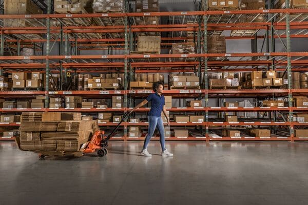 A pallet jack operator pullnig a pallet of boxes in a warehouse