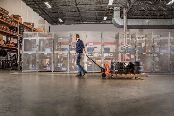 A worker transporting a pallet of tires using a Toyota hand pallet jack