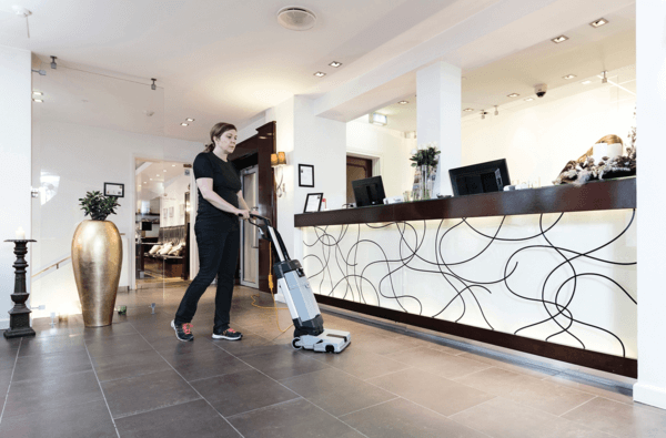 A worker using an Advance SC1000 upright floor scrubber to clean a hotel lobby floor