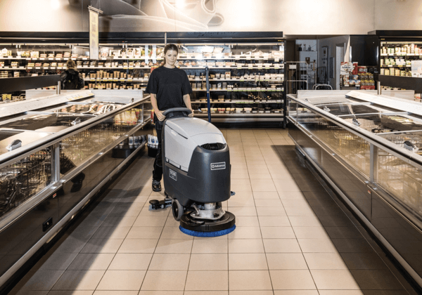 A worker using a floor scrubber to clean a supermarket aisle