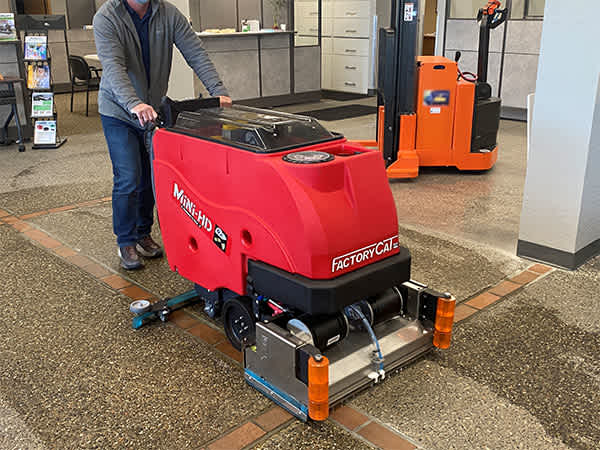 A worker using a Factory Cat Mini-HD walk-behind floor scrubber to clean an office floor