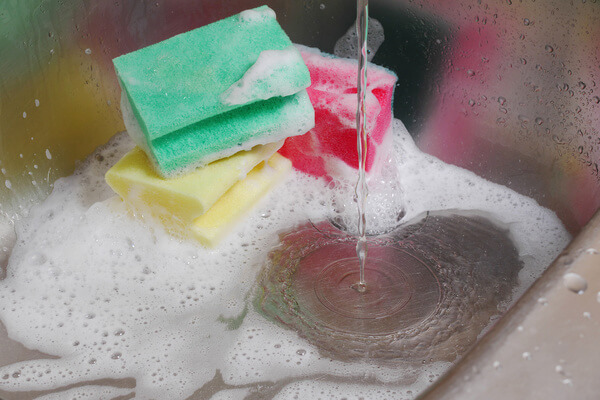 A sink filled with soapy water and scrubbing pads