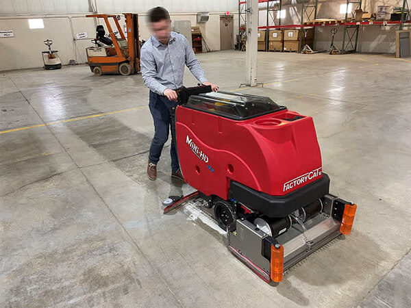 A worker cleaning a warehouse floor with a floor scrubber