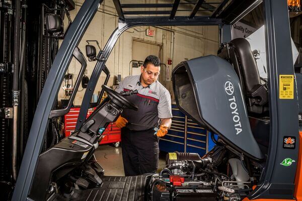 A service technician working under the hood of a Toyota forklift