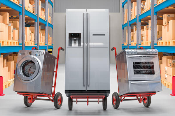 Several household appliances on hand trucks in a warehouse aisle