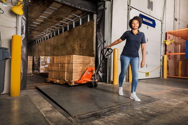 A worker pulling a pallet jack with a load off a semi trailer