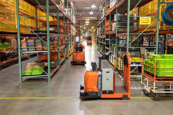 A Toyota AGV tow tractor towing a cart past pallet racking