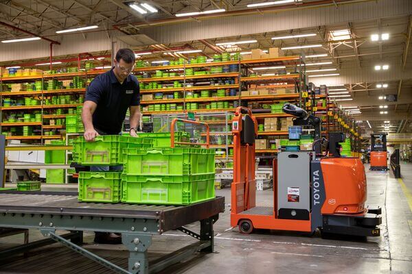 A worker moving crates next to a Toyota AGV tow tractor