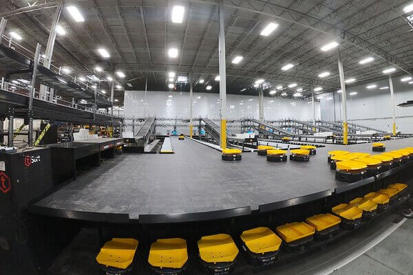 warehouse-amrs-with-tilt-tops Dozens of AMRs with tilt-tops on a warehouse platform