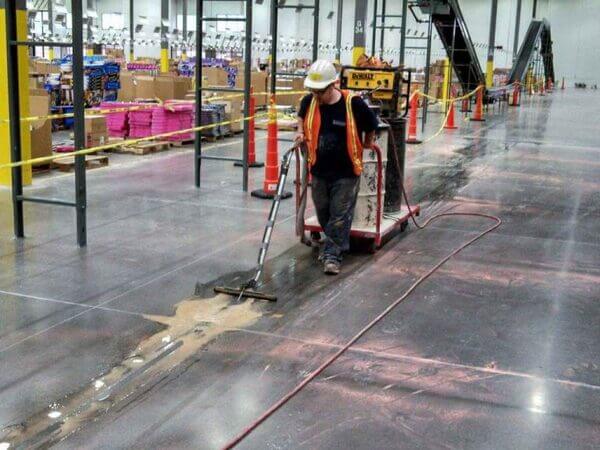 A worker preparing a warehouse floor to bury a wire guidance system