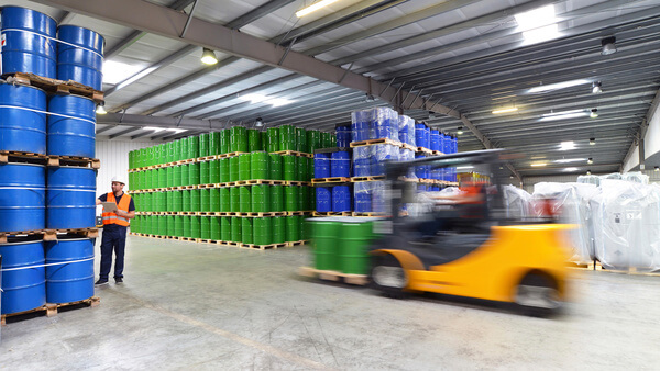A forklift driving through a warehouse with a pallet of barrels on the forks