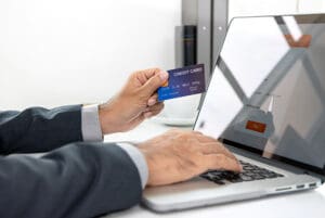 A person holding a credit card while typing on their laptop
