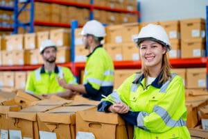 Young warehouse woman worker stand in front of her co-worker wearing safety vests