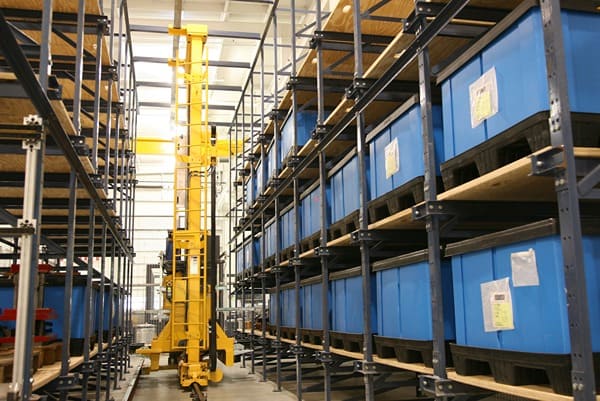 An automatic storage and retrieval system crane moving down a warehouse aisle between racking