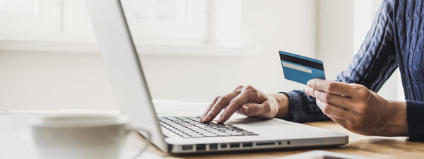 A person holding a credit card while typing on their laptop